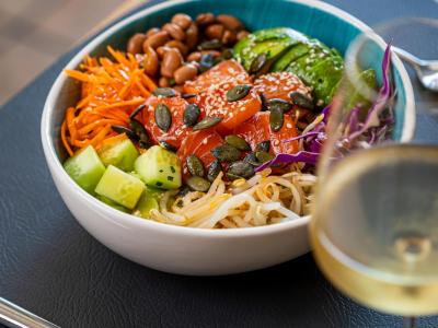 Poke bowl con salmone, avocado e verdure, accompagnata da un bicchiere di vino.