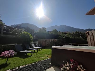 Giardino soleggiato con sdraio, fiori colorati e montagne sullo sfondo.