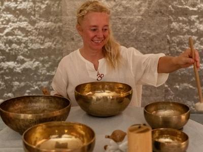 Donna sorridente suona campane tibetane, creando un'atmosfera serena e meditativa.