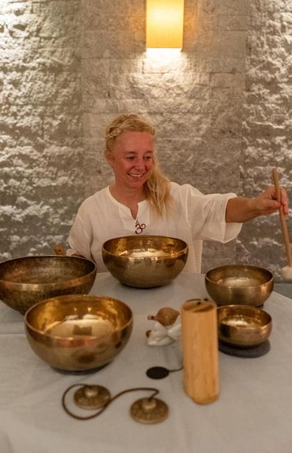Donna sorridente suona campane tibetane, creando un'atmosfera serena e meditativa.
