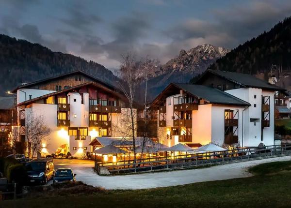 Mountain hotel lit up at night, surrounded by mountains and forests.