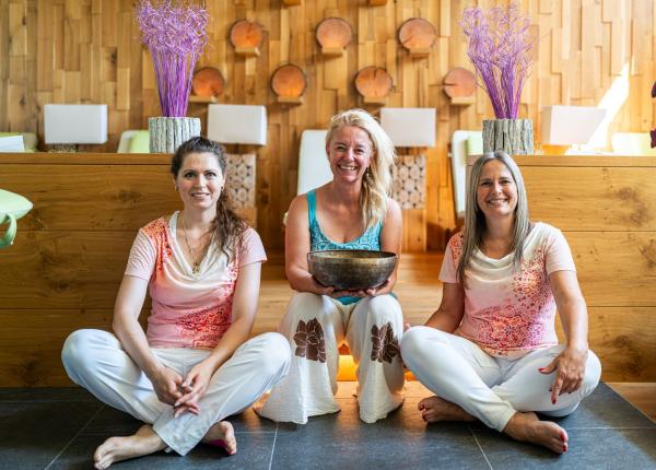 Trois femmes souriantes assises dans un cadre chaleureux avec des décorations en bois.