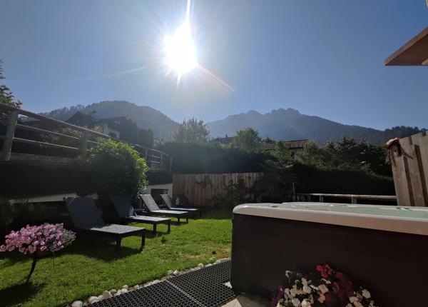 Giardino soleggiato con sdraio, fiori colorati e montagne sullo sfondo.