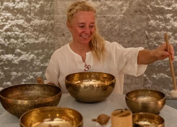 Donna sorridente suona campane tibetane, creando un'atmosfera serena e meditativa.