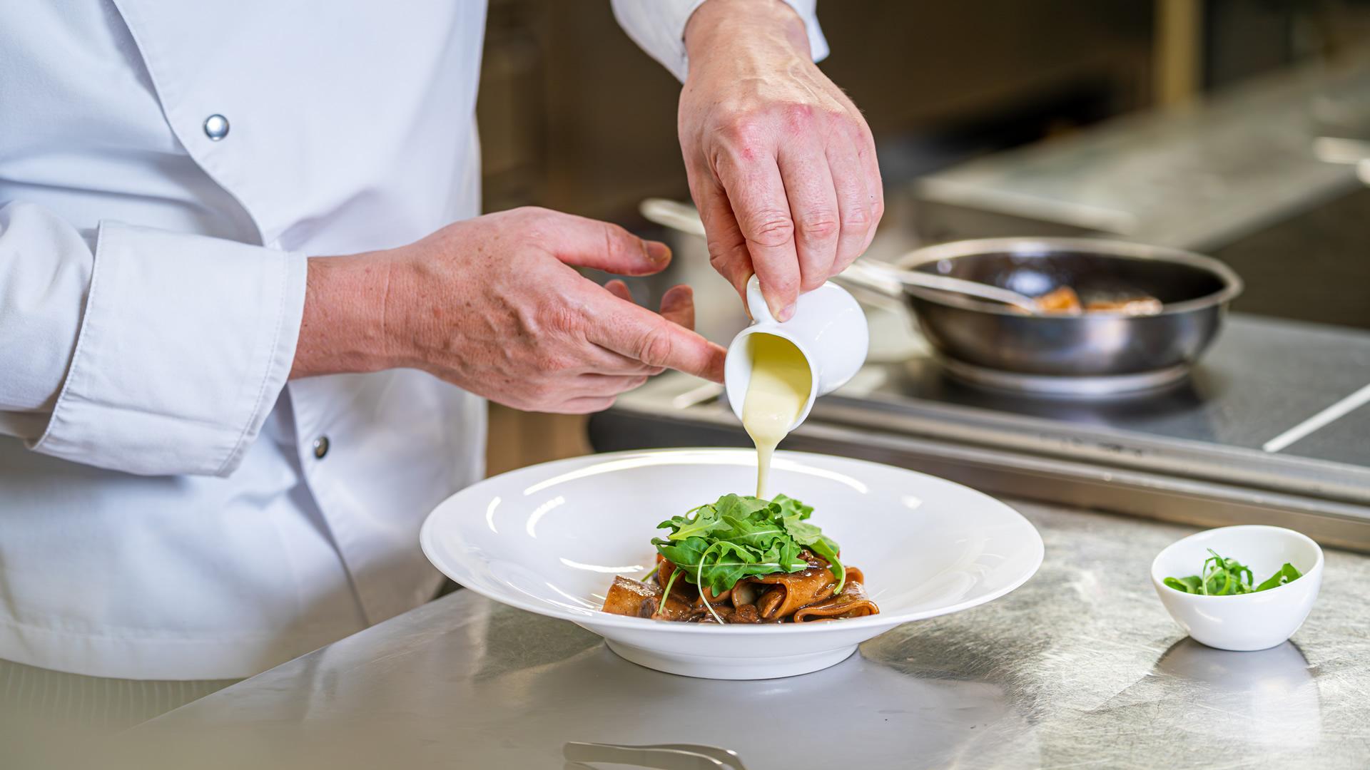 Koch gießt Sauce über Pasta mit Rucola.