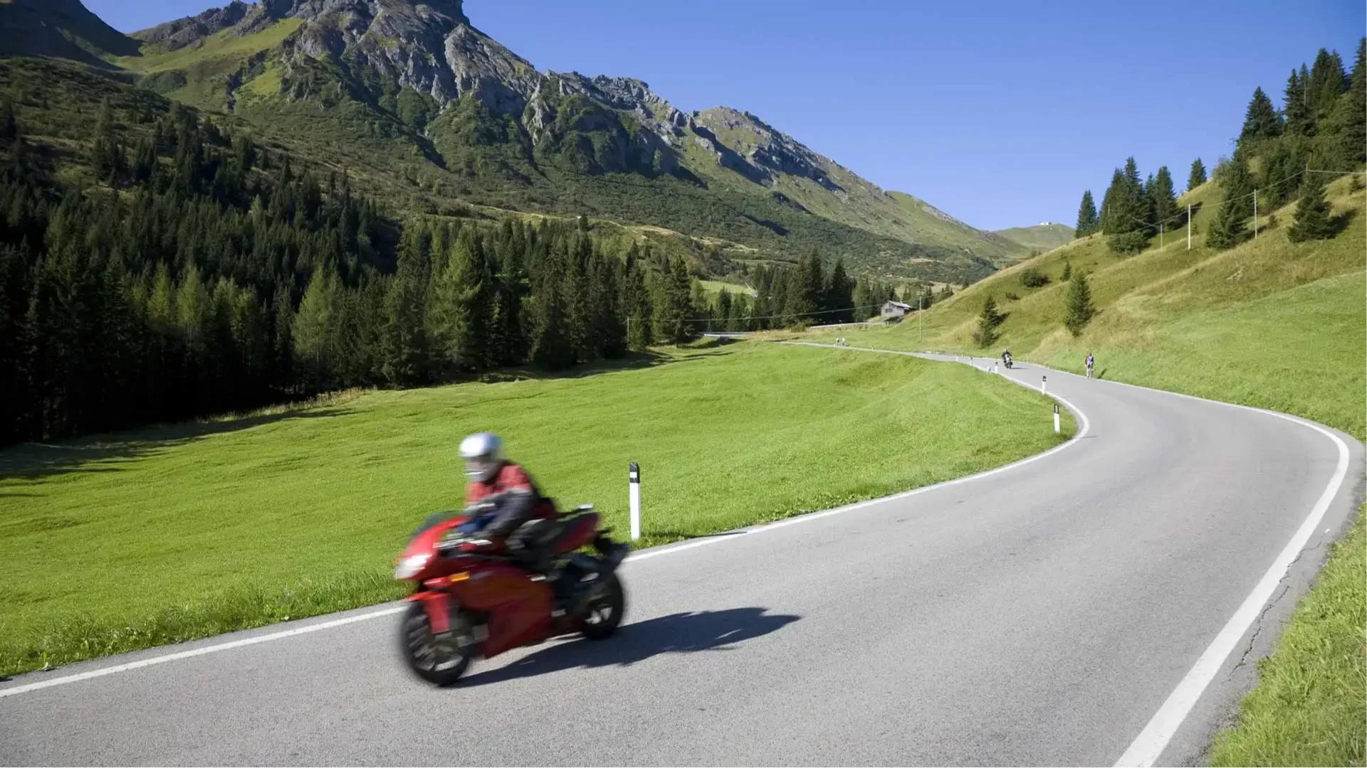 Motociclista su strada di montagna, paesaggio verde e montuoso sullo sfondo.