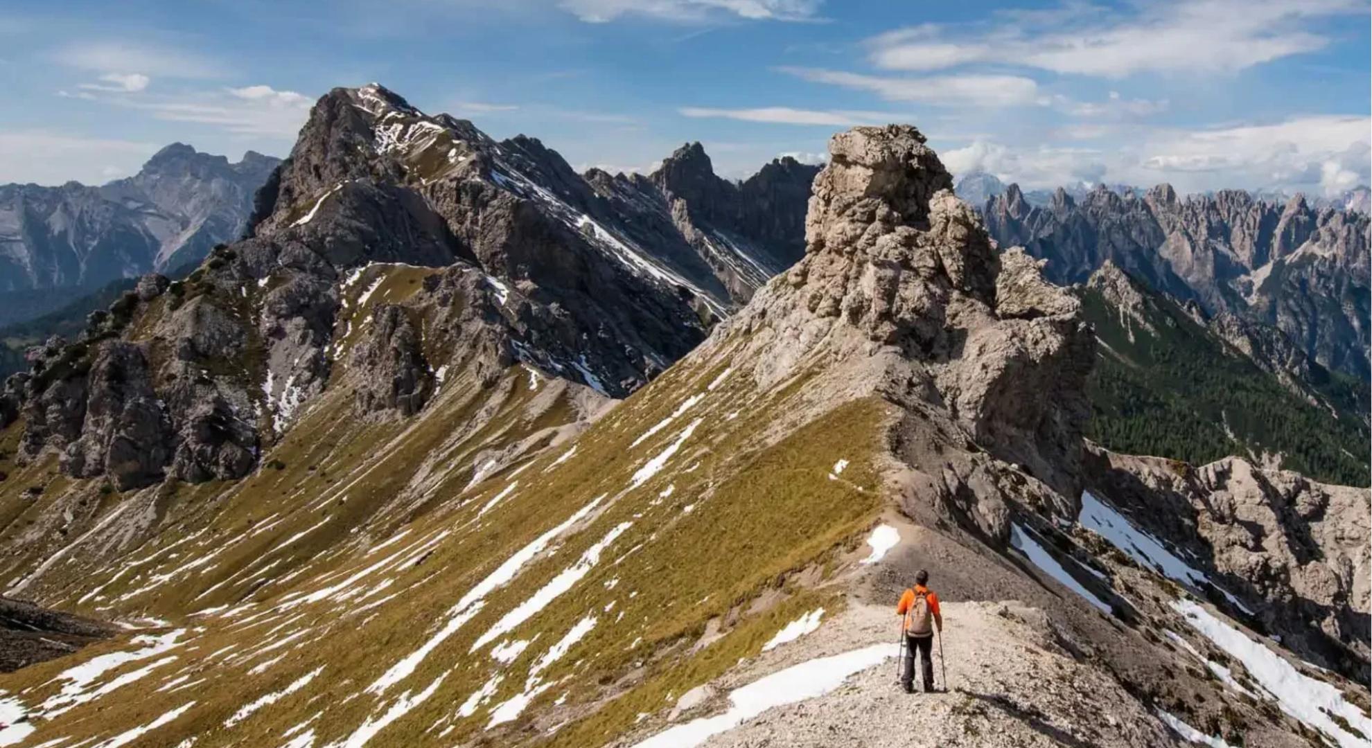 Escursionista su un sentiero di montagna tra rocce e neve, paesaggio alpino mozzafiato.