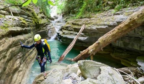 Persona in canyoning esplora un corso d'acqua tra rocce e alberi.