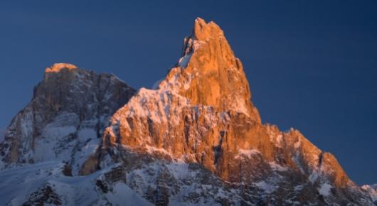 Montagna innevata al tramonto con luce arancione sulle vette.