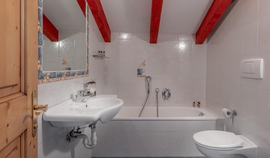 Bagno con vasca, lavandino e travi rosse a vista.