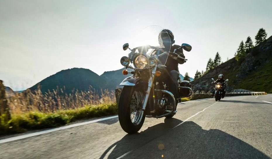 Motociclisti su strada di montagna, immersi in un paesaggio naturale al tramonto.