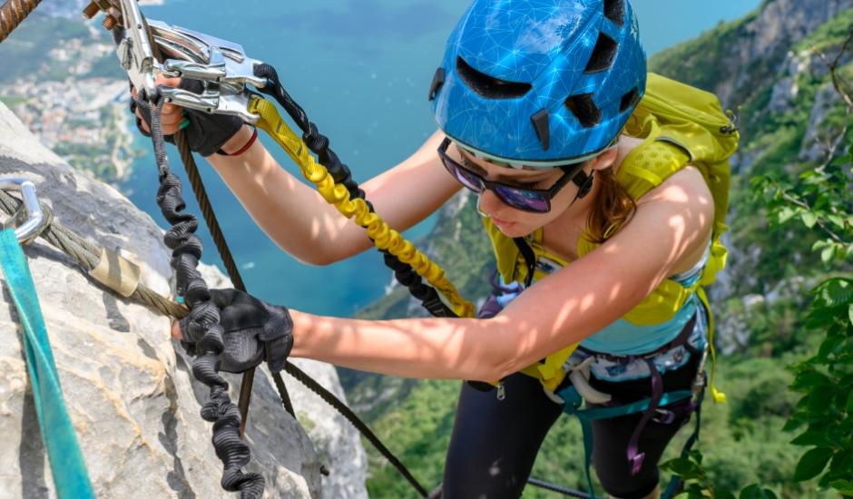 Persona arrampica su via ferrata con casco blu e zaino giallo, vista panoramica.
